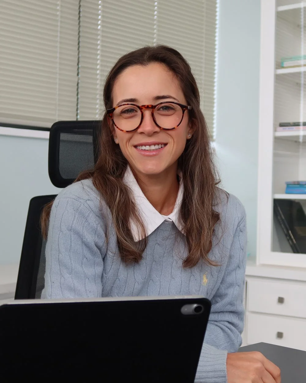 Júlia Fabris em seu consultório, sentada à mesa diante do tablet durante um atendimento online.